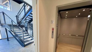 An elevator with a control panel and emergency exit sign, adjacent to a staircase with metal railings. - Clubhouse & Pool Amenities, 40 Mins to Glacier NP (Whitefish)