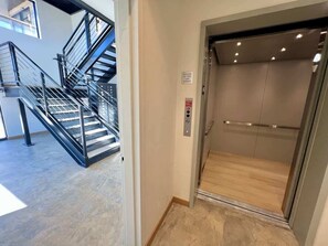 Ein Aufzug mit Bedienfeld und Notausgangsschild neben einer Treppe mit Metallgeländern.