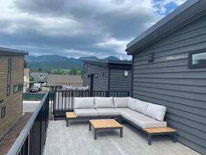 Eine Dachterrasse mit einer Eckcouch und zwei Couchtischen, mit Blick auf ein Wohngebiet und Berge in der Ferne.