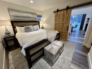 Ein Schlafzimmer mit einem großen Bett, einem Holzkopfende, zwei Nachttischen und Blick ins Freie durch eine Schiebetür.