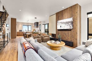 Ein modernes Wohnzimmer mit einem großen Flachbildfernseher, einem Kamin und einer Treppe, die zu einer oberen Ebene führt.