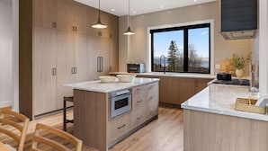 A modern kitchen with wooden cabinets, a large island, and a view of the outdoors. - Luxury Ski-In&Out | Private Spa | Mountain Views (Whitefish)