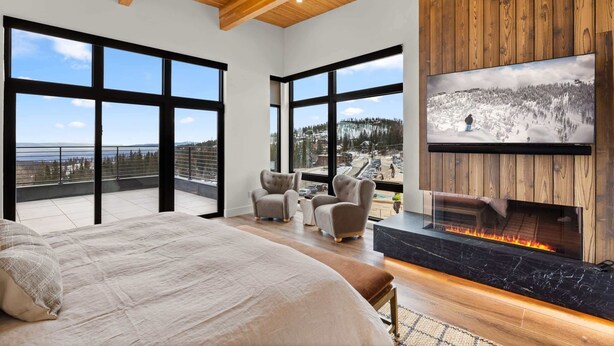 A spacious bedroom with a large bed, a fireplace, and a television mounted on a wooden wall. - Luxury Ski-In&Out | Private Spa | Mountain Views (Whitefish)