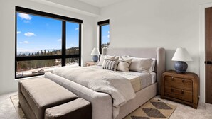 A bedroom with a large bed, two nightstands, a bench, and a view of a snowy landscape. - Luxury Ski-In&Out | Private Spa | Mountain Views (Whitefish)