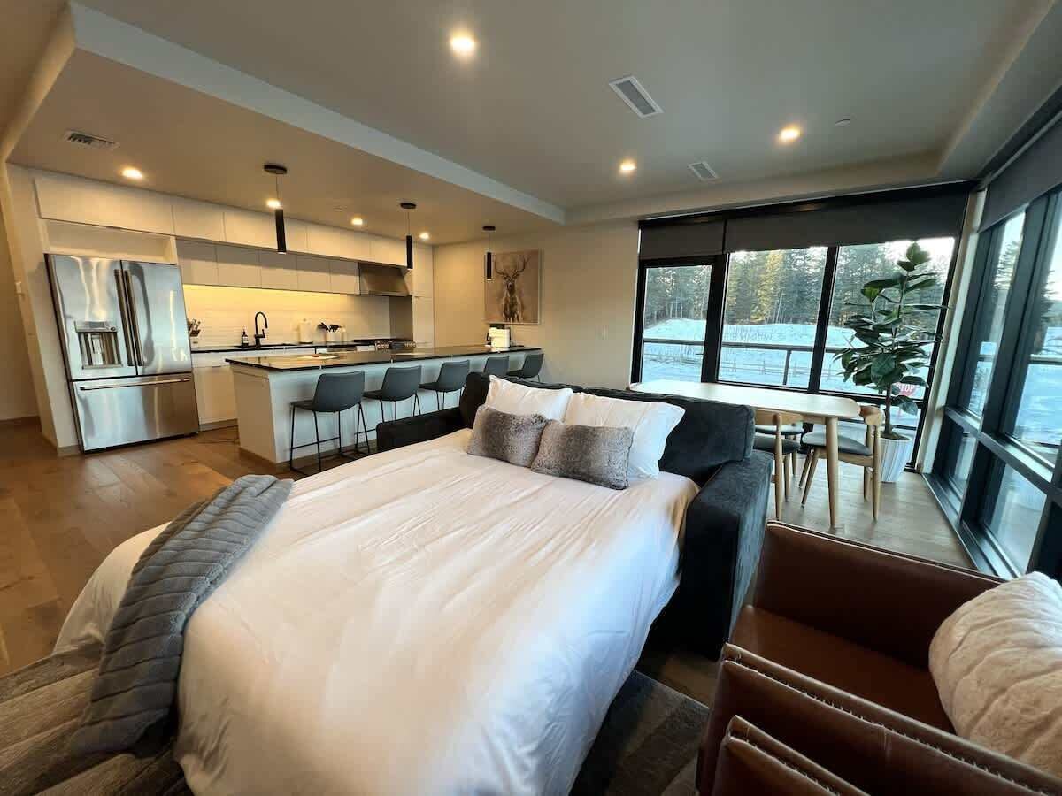 Ein modernes Hotelzimmer mit einem großen Bett, einer Küchenzeile, einem Essbereich und Blick ins Freie.
