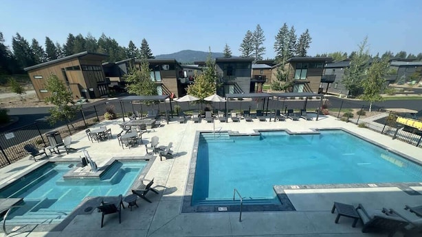 A pool area with multiple pools and lounge chairs, surrounded by modern buildings and trees. - Clubhouse & Pool Amenities, 40 Mins to Glacier NP (Whitefish)