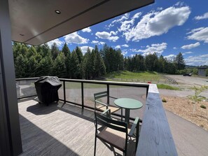 Ein Balkon mit Tisch und Stühlen, mit Blick auf ein bewaldetes Gebiet und einen Parkplatz.