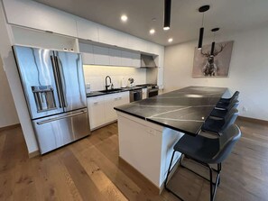 Eine moderne Küche mit einem Edelstahl-Kühlschrank, einer zentralen Kochinsel mit Barhocker, weißen Schränken und einem Hirschbild an der Wand.