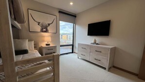A bedroom with a bed, bedside table, lamp, a mounted TV, a dresser, and a large window with a city view. - Clubhouse & Pool Amenities, 40 Mins to Glacier NP (Whitefish)