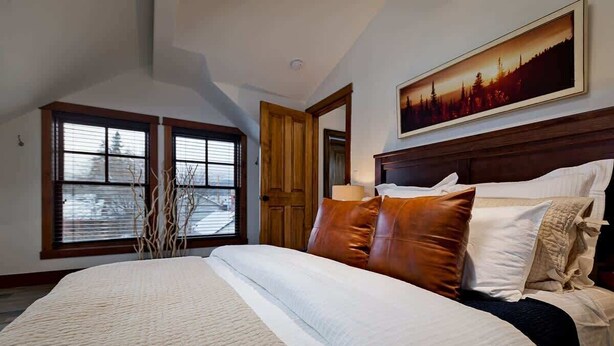 A bedroom with a large bed, wooden headboard, and a painting on the wall. - Downtown Condo, Sleeps 7, 35 Mins to Glacier Park (Whitefish)