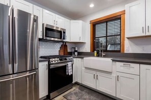 A modern kitchen with stainless steel appliances, white cabinetry, a built-in oven, and a window with blinds. - Downtown Condo, Sleeps 7, 35 Mins to Glacier Park (Whitefish)
