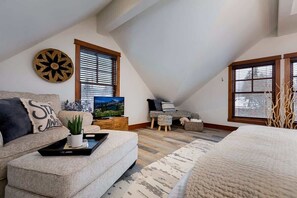 A loft bedroom with a sloped ceiling, a large bed, a sofa, a TV, and a painting. - Downtown Condo, Sleeps 7, 35 Mins to Glacier Park (Whitefish)