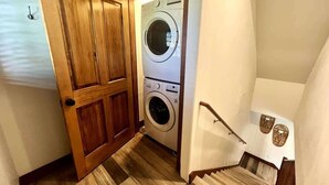A laundry room with a washing machine and dryer, wooden flooring, and a staircase with a handrail. - Downtown Condo, Sleeps 7, 35 Mins to Glacier Park (Whitefish)