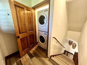 Ein Waschraum mit Waschmaschine und Trockner, Holzboden und einer Treppe mit Handlauf.