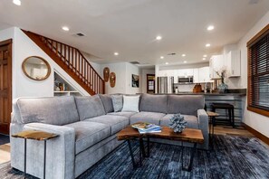 A modern living room with a grey sectional sofa, a wooden coffee table, and a staircase leading to an upper level. - Downtown Condo, Sleeps 7, 35 Mins to Glacier Park (Whitefish)