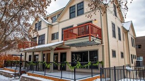 A two-story building with a covered front porch, a red balcony, and a snow-covered ground. - Downtown Condo, Sleeps 7, 35 Mins to Glacier Park (Whitefish)