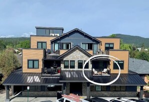 Un edificio moderno de varios pisos, con un balcón destacado, un área de estar al aire libre techada y una entrada de garaje visible.