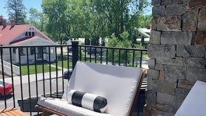 A patio with two lounge chairs, a wooden table, and a stone wall. - Rooftop Patio, Downtown, 40 Mins to Glacier Park (Whitefish)