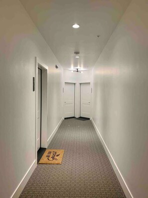 A hallway with a patterned carpet, white walls, and a ceiling light. - Rooftop Patio, Downtown, 40 Mins to Glacier Park (Whitefish)