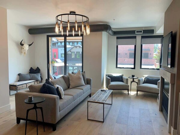 Una sala de estar moderna con un sofá, una mesa de centro, sillas, ventanas amplias con vista a la ciudad, un televisor montado en la pared y una decoración con cráneo de toro.