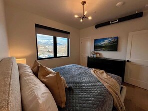 A bedroom with a bed, a desk, a chair, a window with a city view, and a ceiling fan. - Rooftop Patio, Downtown, 40 Mins to Glacier Park (Whitefish)