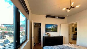 A bedroom with a large window, a bed, a dresser, a painting, and a closet. - Rooftop Patio, Downtown, 40 Mins to Glacier Park (Whitefish)
