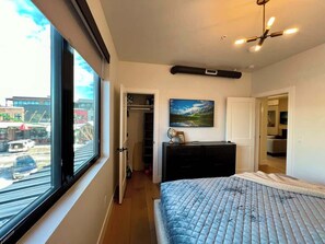 Ein Schlafzimmer mit großem Fenster, einem Bett, einem Schminktisch, einem Gemälde und einem Kleiderschrank.