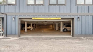 A building with a garage entrance, a yellow clearance sign, and two cars parked inside. - Rooftop Patio, Downtown, 40 Mins to Glacier Park (Whitefish)