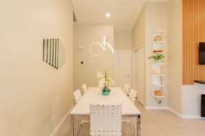 Un comedor moderno con una mesa larga, sillas, un jarrón de flores y un aplique en la pared.