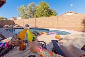 Ein Garten mit Swimmingpool, Liegestühlen und einer Person, die ein Getränk hält.