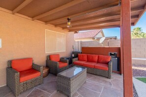 Ein überdachter Patio-Bereich mit Korbmöbeln und einem Grill.