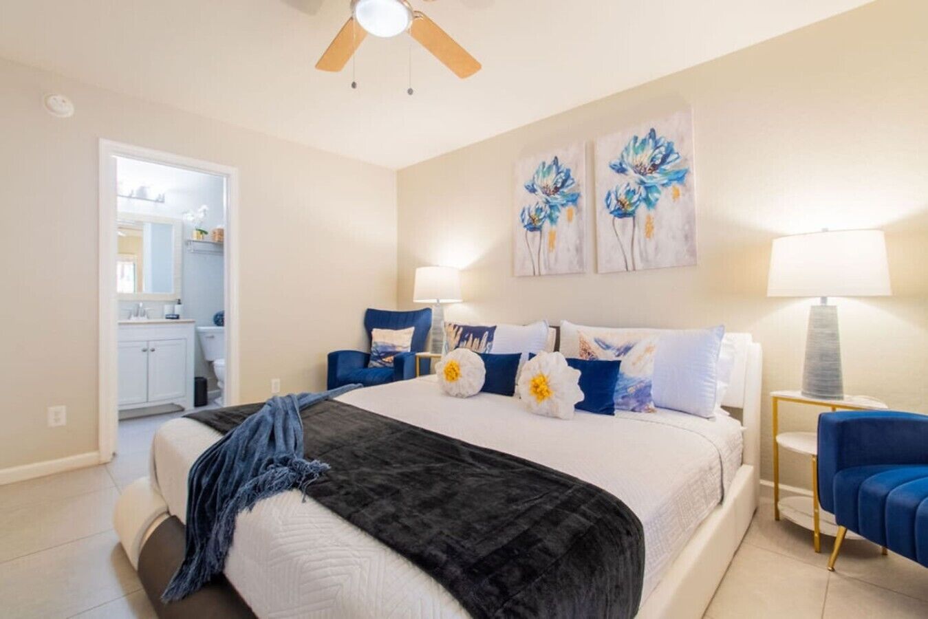 Une chambre à coucher avec un lit, un ventilateur de plafond, une table de chevet, une lampe et des œuvres d’art accrochées au mur.