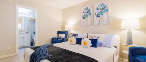 A bedroom with a bed, a ceiling fan, a nightstand, a lamp, and artwork on the wall.
