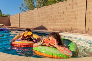 Una piscina con dos personas en flotadores, una sosteniendo una rodaja de naranja y la otra una rodaja de pomelo.