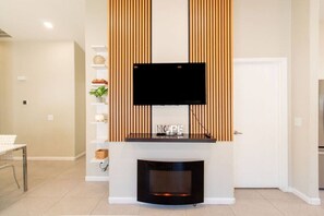 A modern living room with a flat-screen TV mounted above a fireplace, a white door, and a tiled floor. - Cozy Desert Escape with Modern ComfortsVilla (Casa Grande)