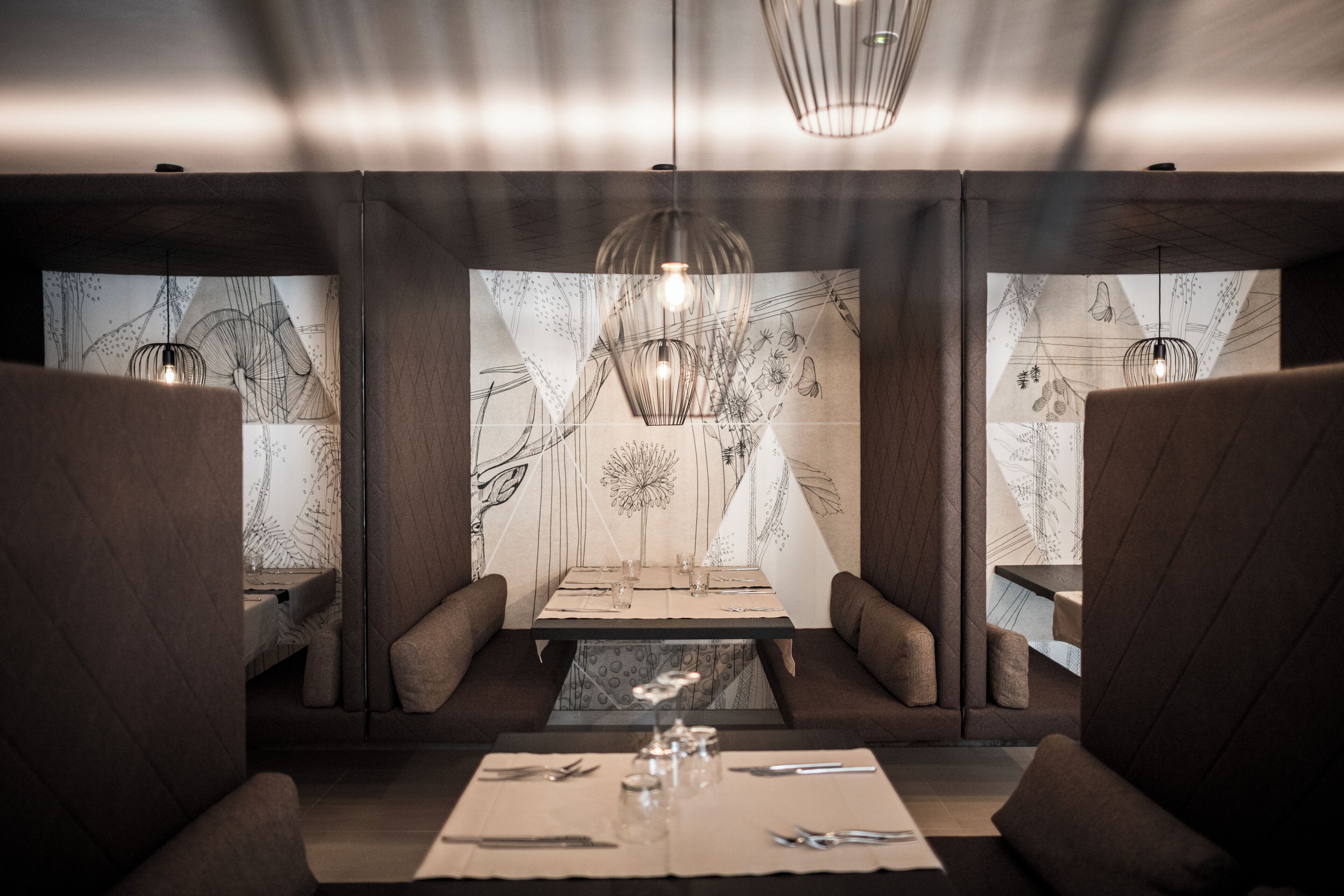 A restaurant interior with a table set for two, a patterned wall, and pendant lighting.