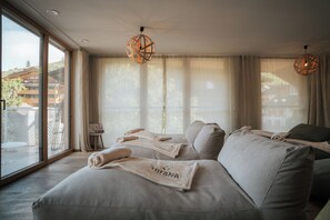 A modern bedroom with a large bed, a small table, and a view of a building outside. - Hotel Tofana - Explorer's Home (San Cassiano)