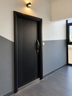 A modern door with a vertical panel design, a handle, and a light fixture above it.