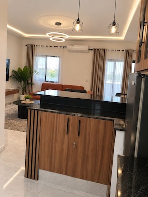 A modern kitchen with a central island, pendant lighting, and a view to the living area.