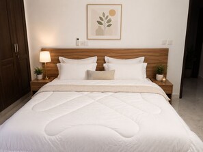 A neatly made bed with a wooden headboard, a bedside lamp, and a framed artwork on the wall.