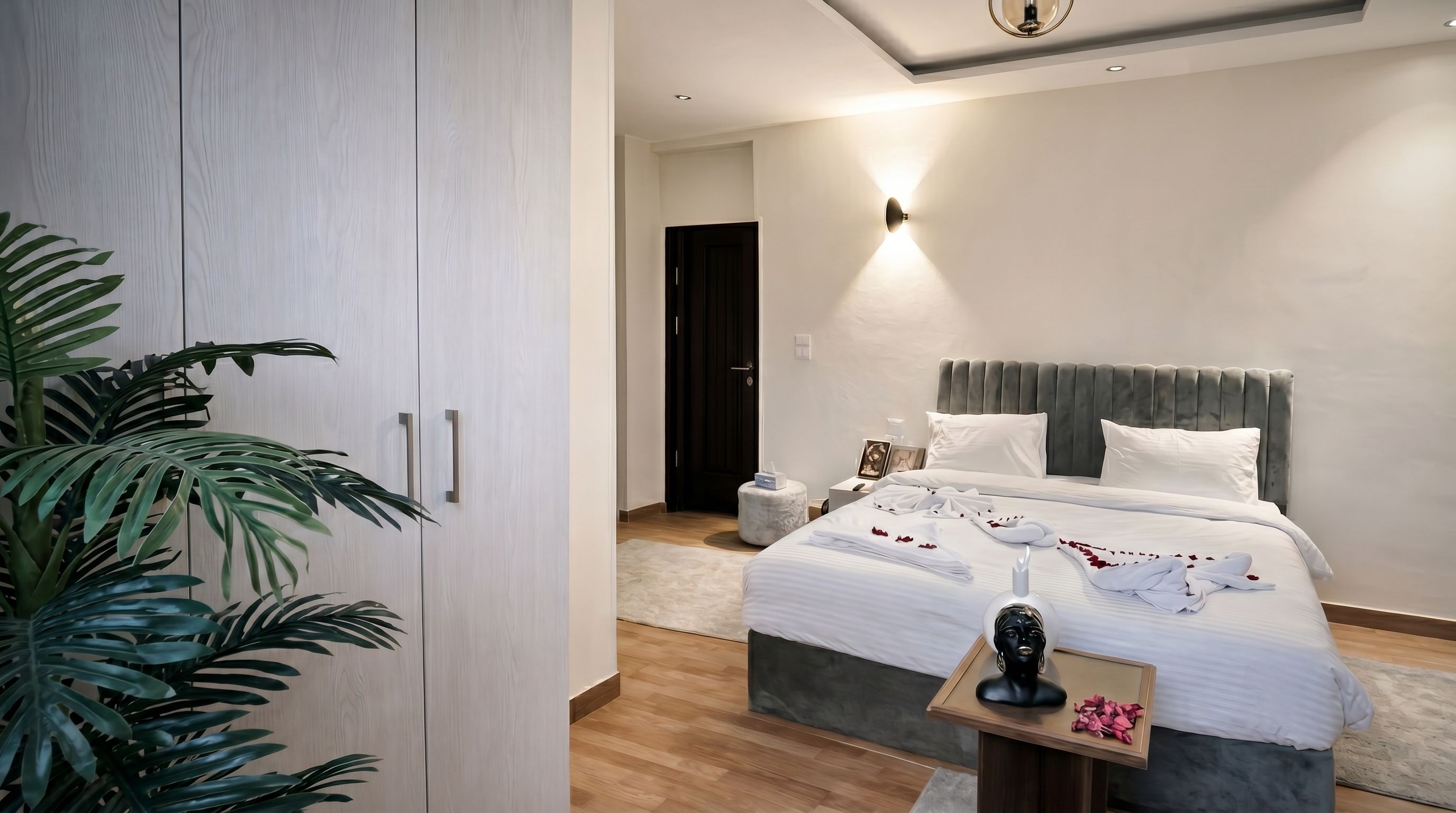 Una habitación de hotel moderna con una cama grande, mesitas de noche, un armario y una planta en maceta.