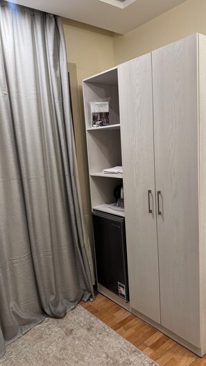 A room with a grey wardrobe, a small black appliance, and a grey curtain.