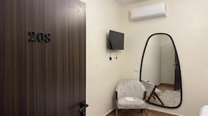 A room with a wooden door marked '208', a grey armchair, a flat-screen TV mounted on the wall, and a large mirror. - Villa Golden Sunset Pyramids Inn (Giza)