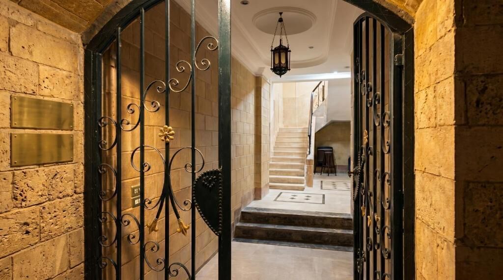A grand entrance with a wrought iron gate, a stone wall, and a staircase leading to an upper level.