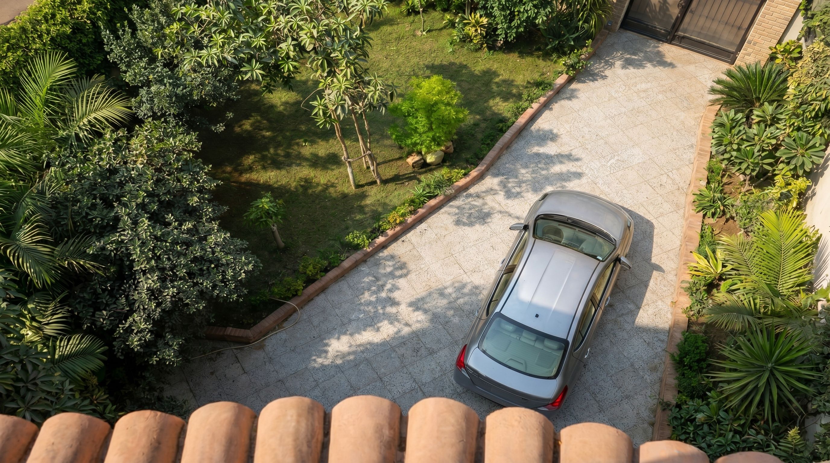 Une voiture est garée sur une allée menant à une maison, avec un jardin et un bâtiment en arrière-plan.