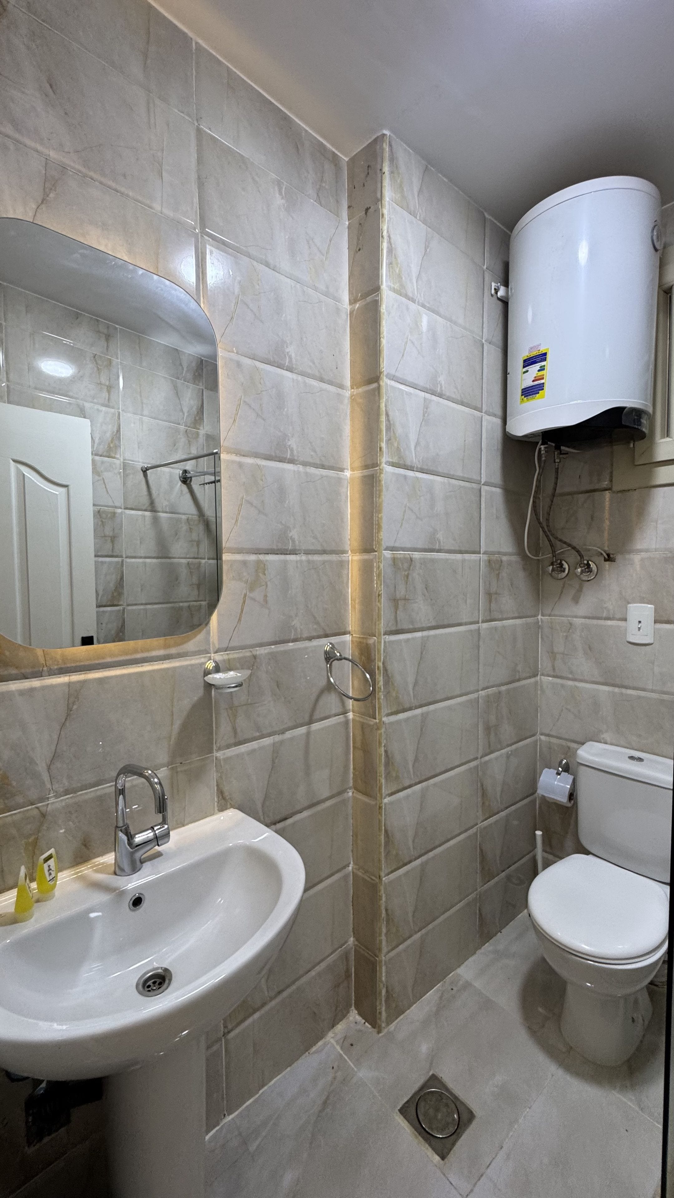 A bathroom with a sink, mirror, toilet, and a water heater.