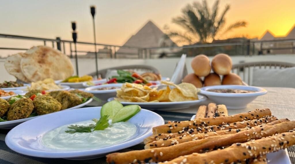 A table with various dishes, including falafel, chips, and bread, with a view of pyramids in the background.