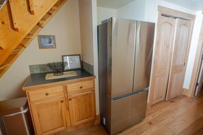 A kitchen with wooden cabinets, a stainless steel refrigerator, and a wooden door. - Columbine 1302! Ski-In/Out! Hot Tub! Views! (Crested Butte)