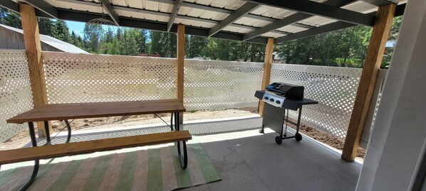 A covered outdoor area with a grill and a bench.