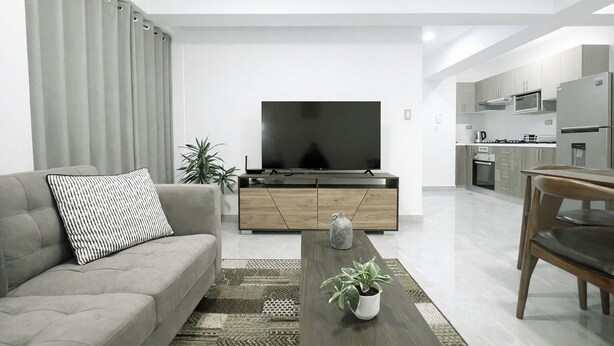 A modern living room with a sofa, TV, wooden cabinet, and a dining area with a table and chairs. - Apartment in Yanahuara: Modern, Central, and Fully Equipped (Yanahuara)